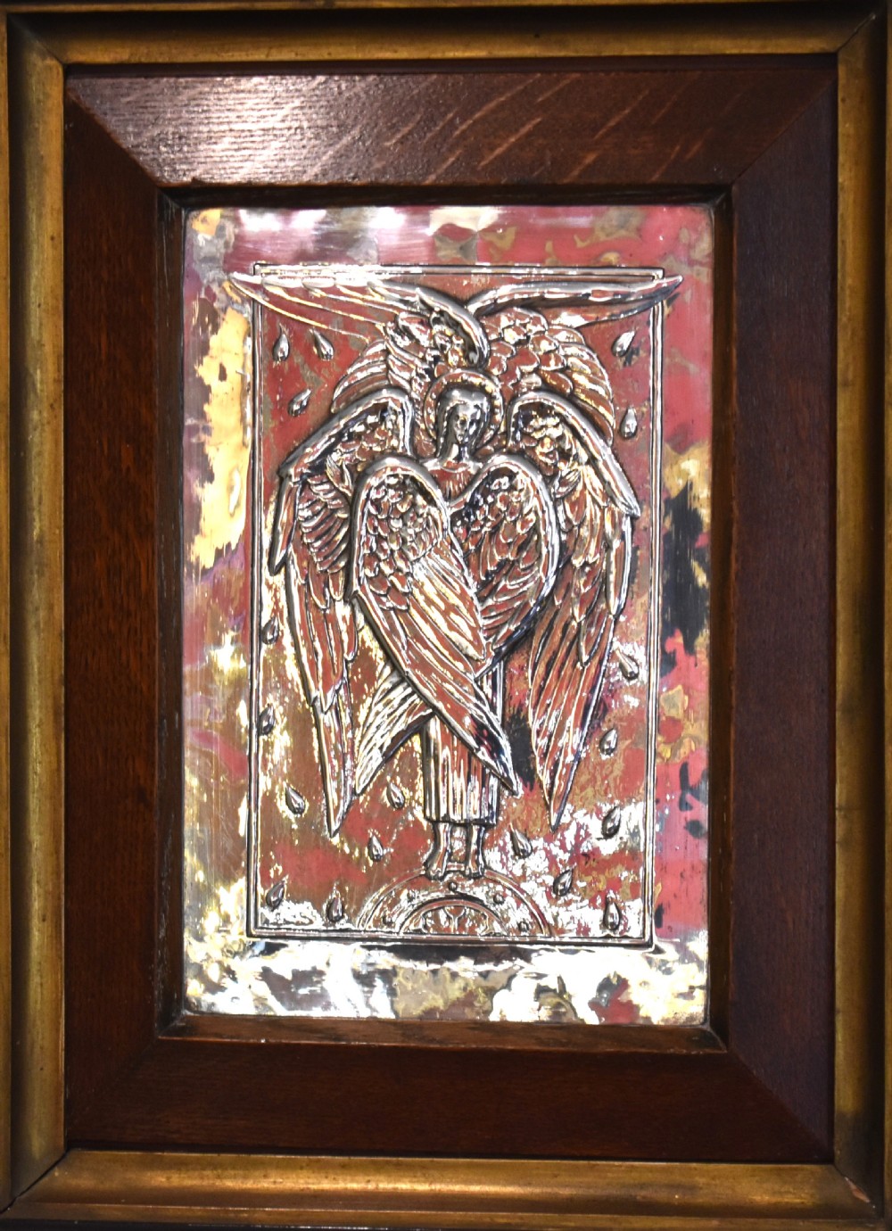 An Arts and Crafts relief plaque depicting a multi-winged angel in hammered silvered metal, set within a multi-tiered ebonised and oak frame. View II