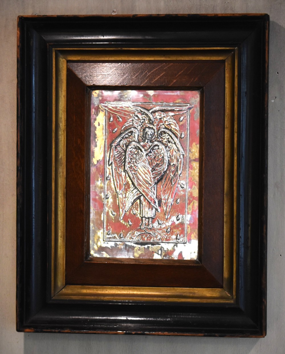 An Arts and Crafts relief plaque depicting a multi-winged angel in hammered silvered metal, set within a multi-tiered ebonised and oak frame. View III