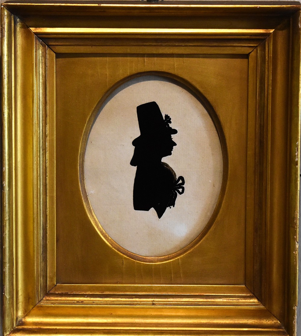A profile silhouette painting of a figure in a top hat set within an oval mount inside a rectangular gilded wood frame. View III