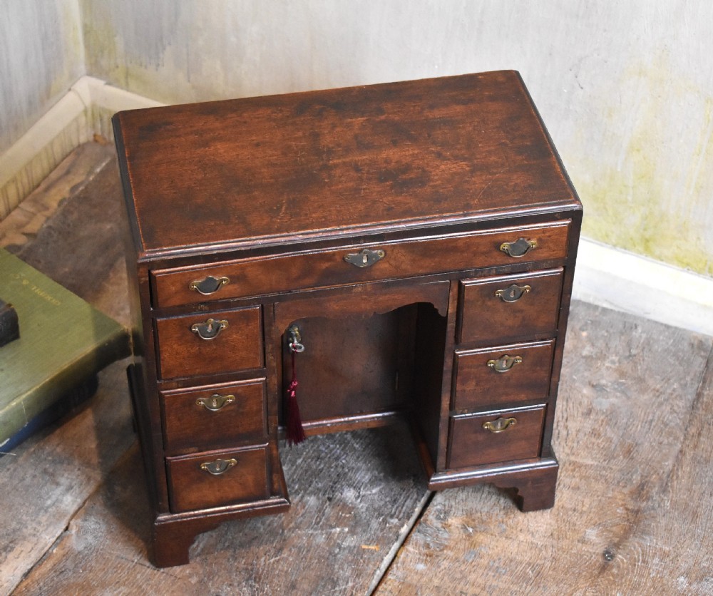 A miniature mahogany kneehole desk featuring a top drawer, six pedestal drawers, a central recessed cupboard, brass hardware, and bracket feet. View II