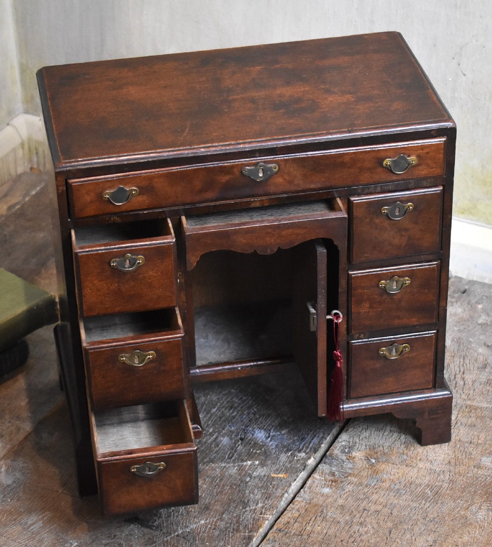 A miniature mahogany kneehole desk featuring a top drawer, six pedestal drawers, a central recessed cupboard, brass hardware, and bracket feet. View III