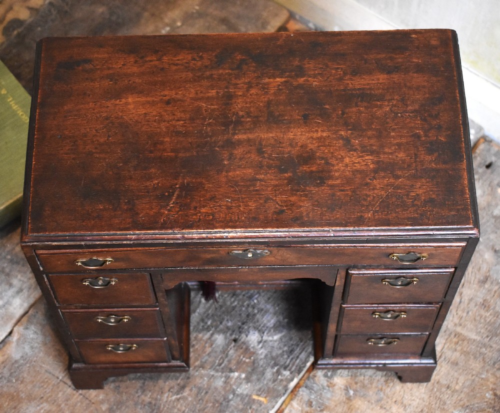 A miniature mahogany kneehole desk featuring a top drawer, six pedestal drawers, a central recessed cupboard, brass hardware, and bracket feet. View IV