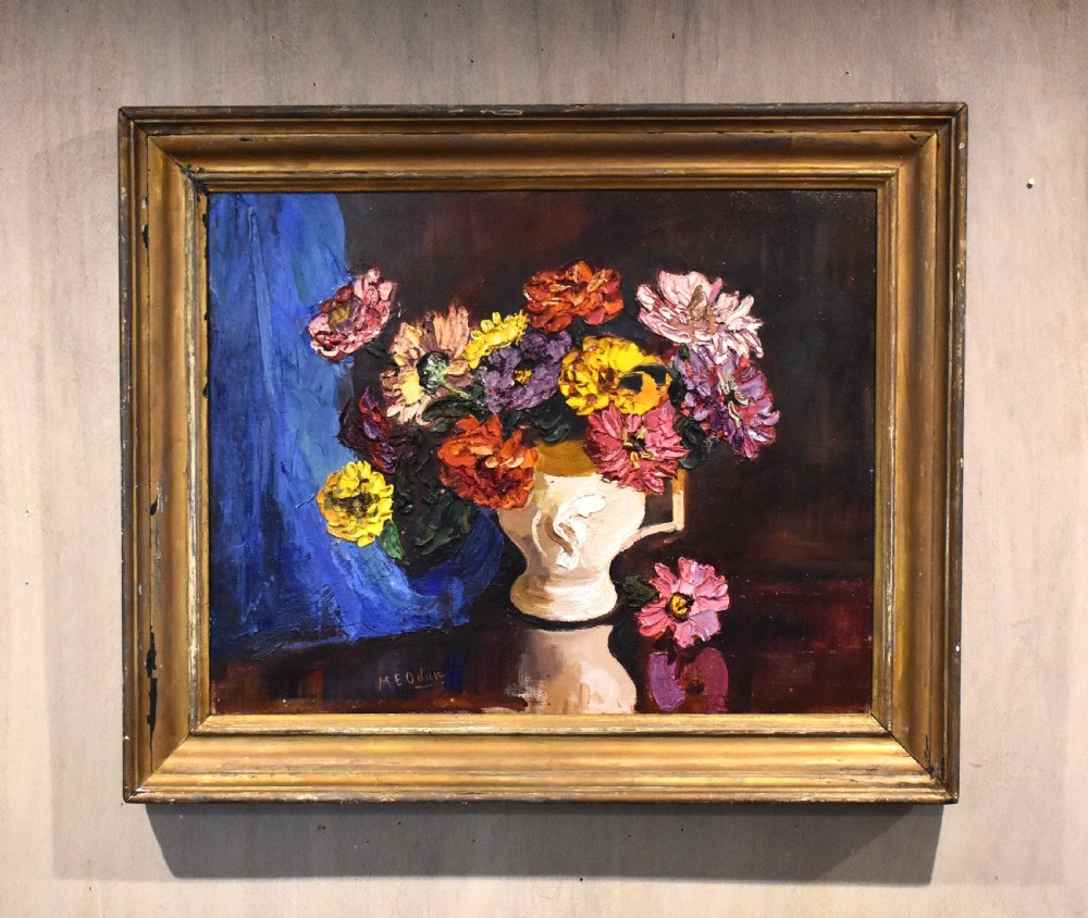 A framed oil painting featuring a vase filled with colourful flowers beside a draped blue cloth set against a dark background.