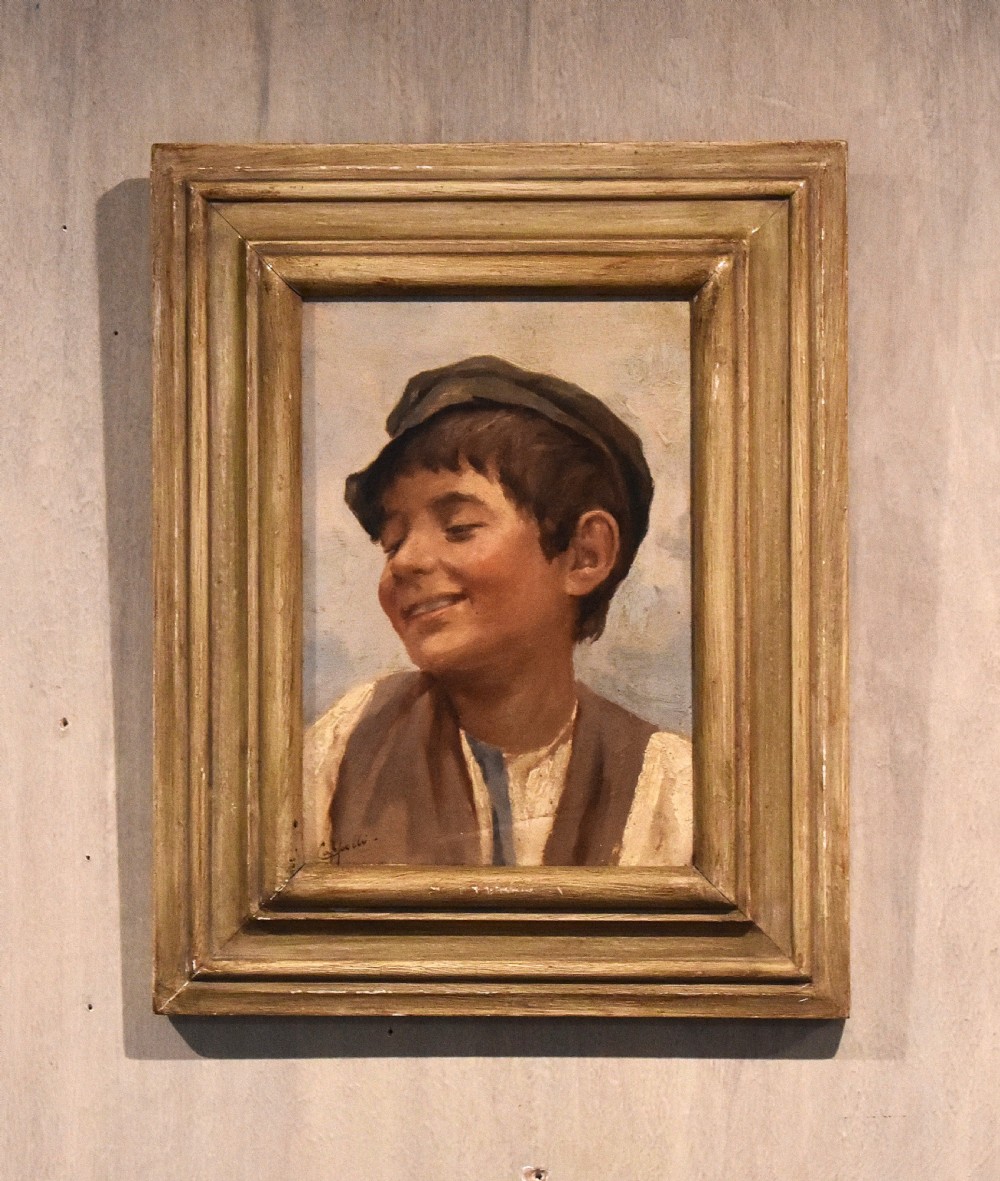 A framed oil painting depicting a smiling young boy wearing a cap and brown vest set within a moulded wooden frame.