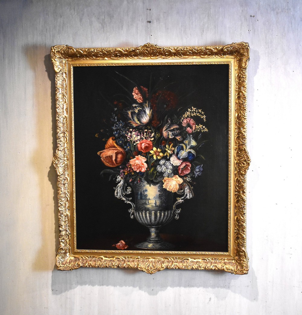An eighteenth-century style floral still life oil painting depicting a colourful bouquet in a detailed urn, housed within an ornate carved giltwood frame.