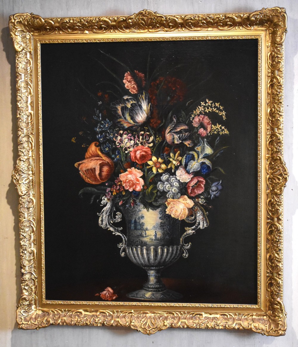 An eighteenth-century style floral still life oil painting depicting a colourful bouquet in a detailed urn, housed within an ornate carved giltwood frame. View II