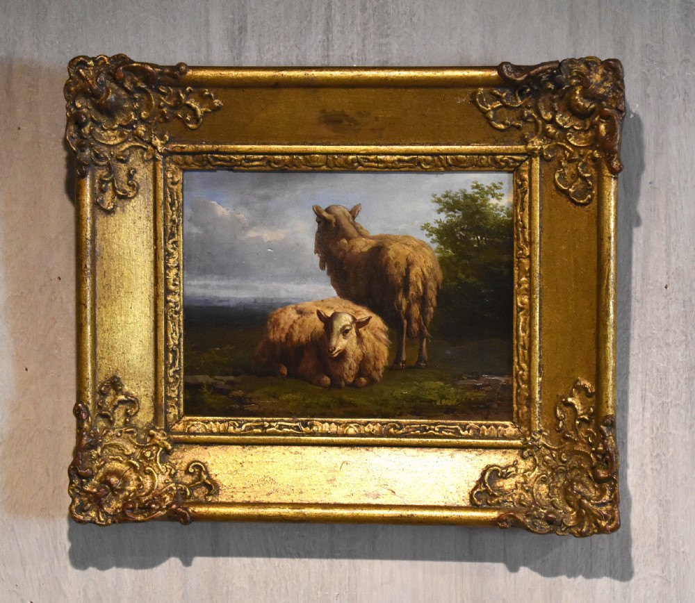 A small 19th-century pastoral oil painting depicting two sheep in a landscape, set within an ornate gilded frame with scrolled corner detailing.