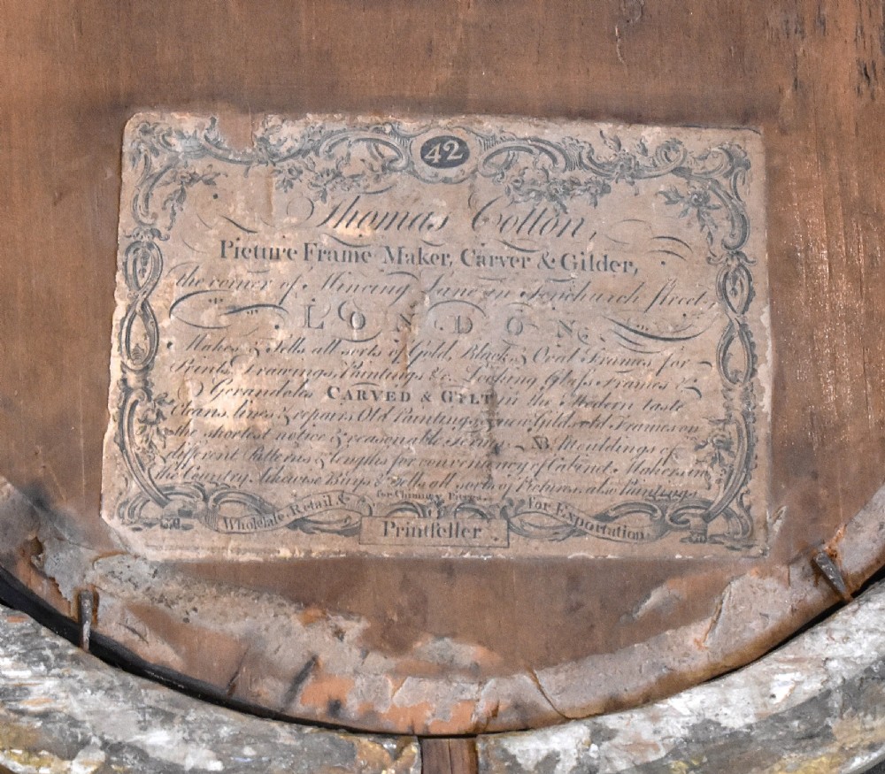 An oval Georgian giltwood mirror featuring a carved urn surmount filled with wheat sheaves, trailing floral husk swags, and an acanthus leaf bottom finial. View VII