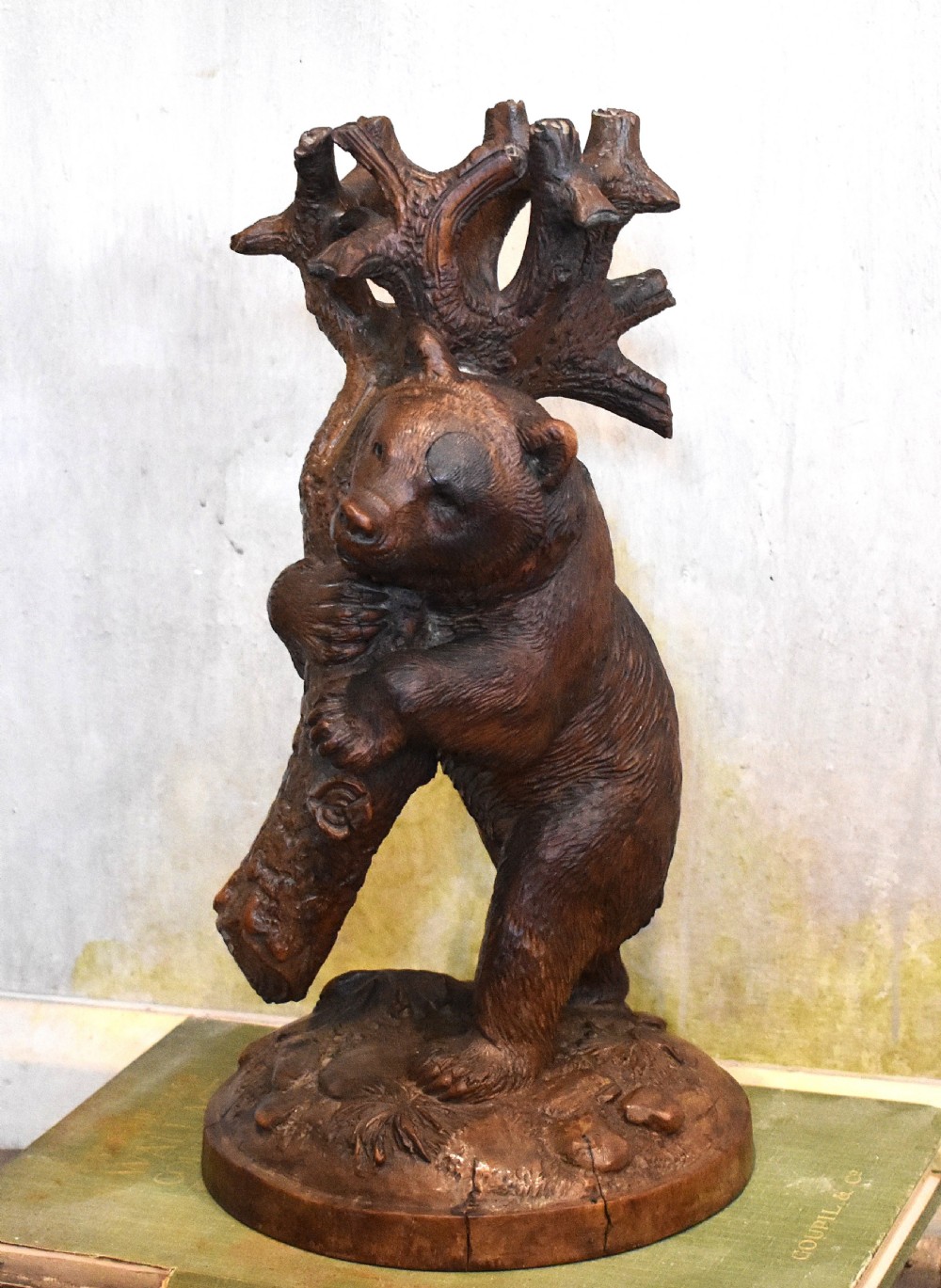 A dark hand-carved wooden sculpture depicting a bear climbing a rustic tree trunk mounted on a circular moulded base.
