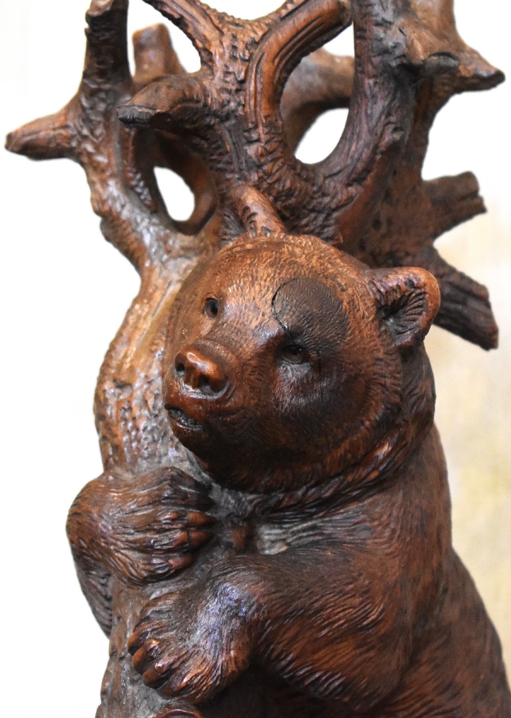 A dark hand-carved wooden sculpture depicting a bear climbing a rustic tree trunk mounted on a circular moulded base. View V