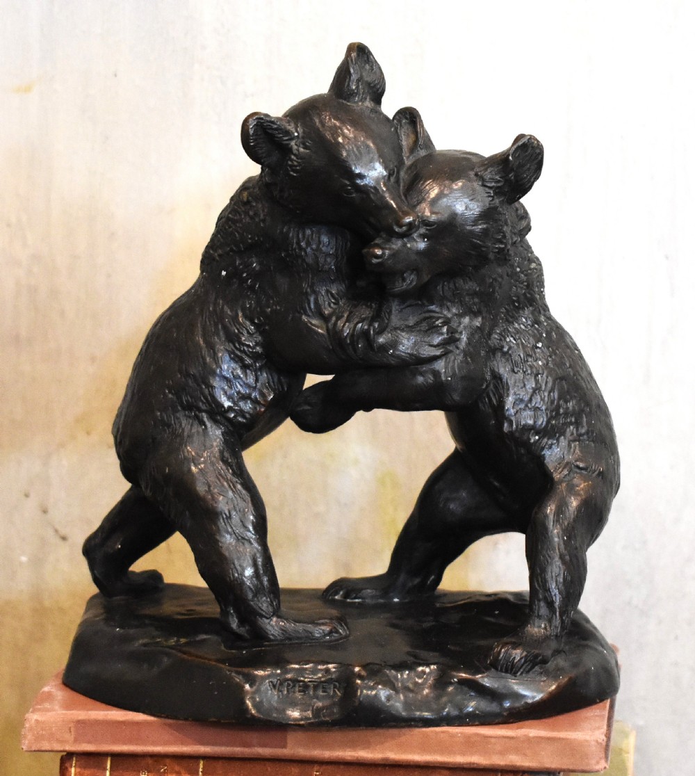 A dark patinated bronze sculpture depicting two play-fighting bear cubs standing on an integral naturalistic bronze base.