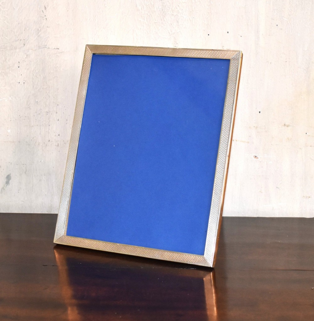 An upright rectangular Art Deco silver picture frame with textured engine-turned detailing around the border and a blue insert.