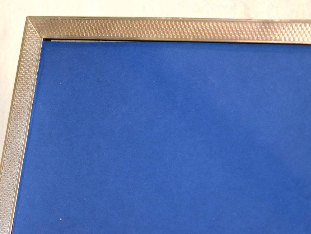 An upright rectangular Art Deco silver picture frame with textured engine-turned detailing around the border and a blue insert. View IV