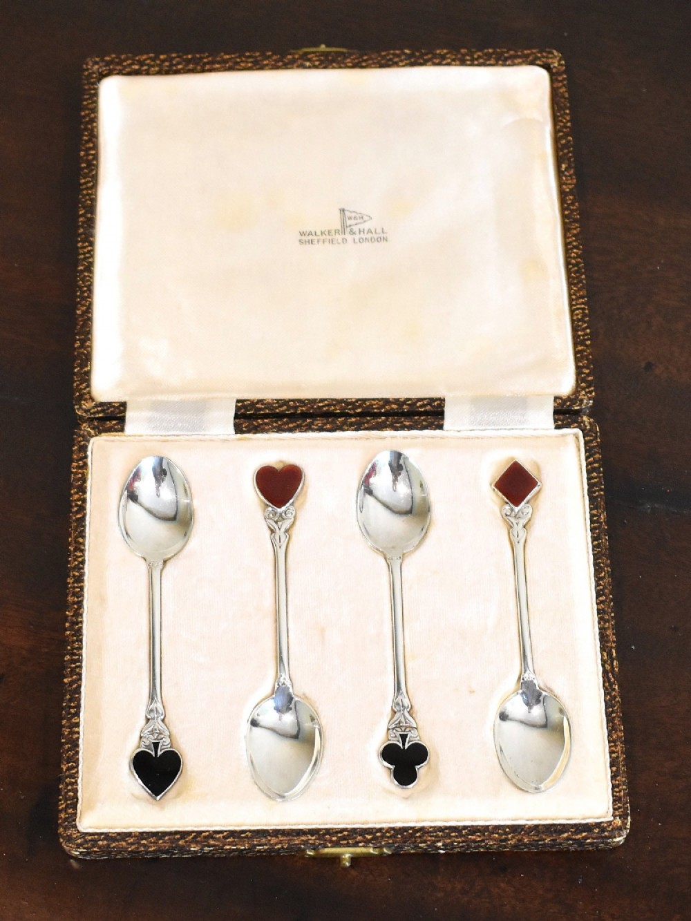 A boxed set of four silver teaspoons featuring red and black enamel playing card suits on the terminals.