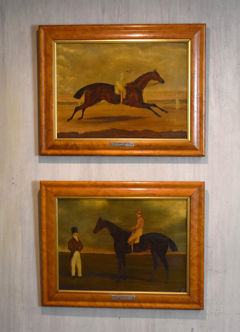 A vertical pair of framed antique sporting prints depicting racehorses and jockeys set in golden maple frames with brass title plaques.