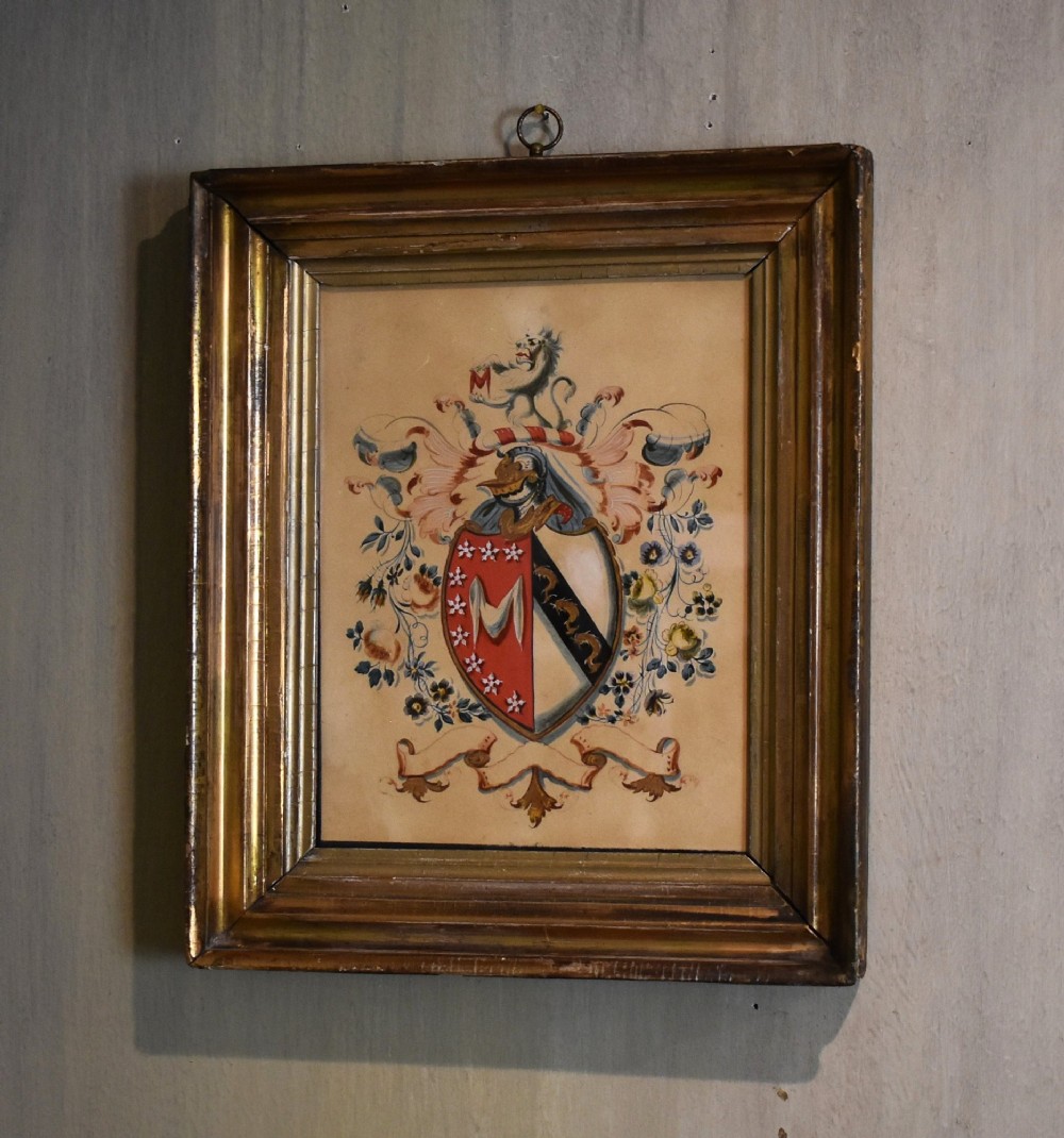 A framed nineteenth-century watercolour painting depicting an intricate heraldic coat of arms with a shield, crest, and floral flourishes inside a gilded wooden frame.