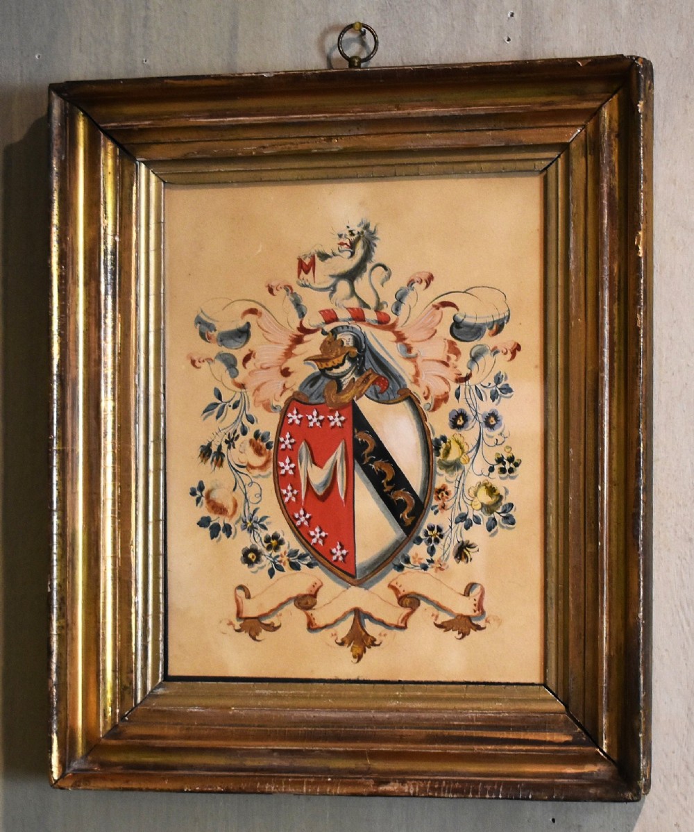 A framed nineteenth-century watercolour painting depicting an intricate heraldic coat of arms with a shield, crest, and floral flourishes inside a gilded wooden frame. View II