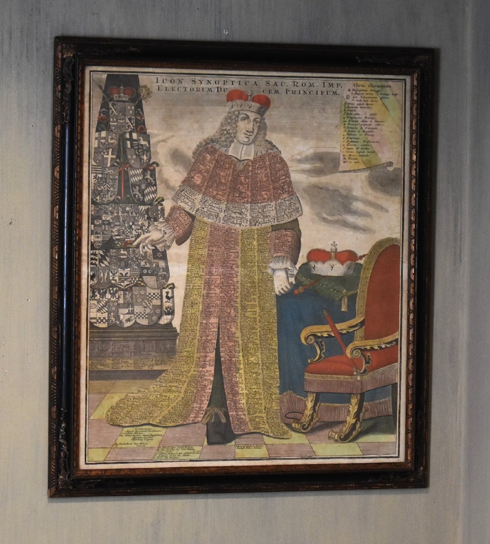 An 18th-century framed print featuring a standing figure in ceremonial robes alongside heraldic shields and Latin text.