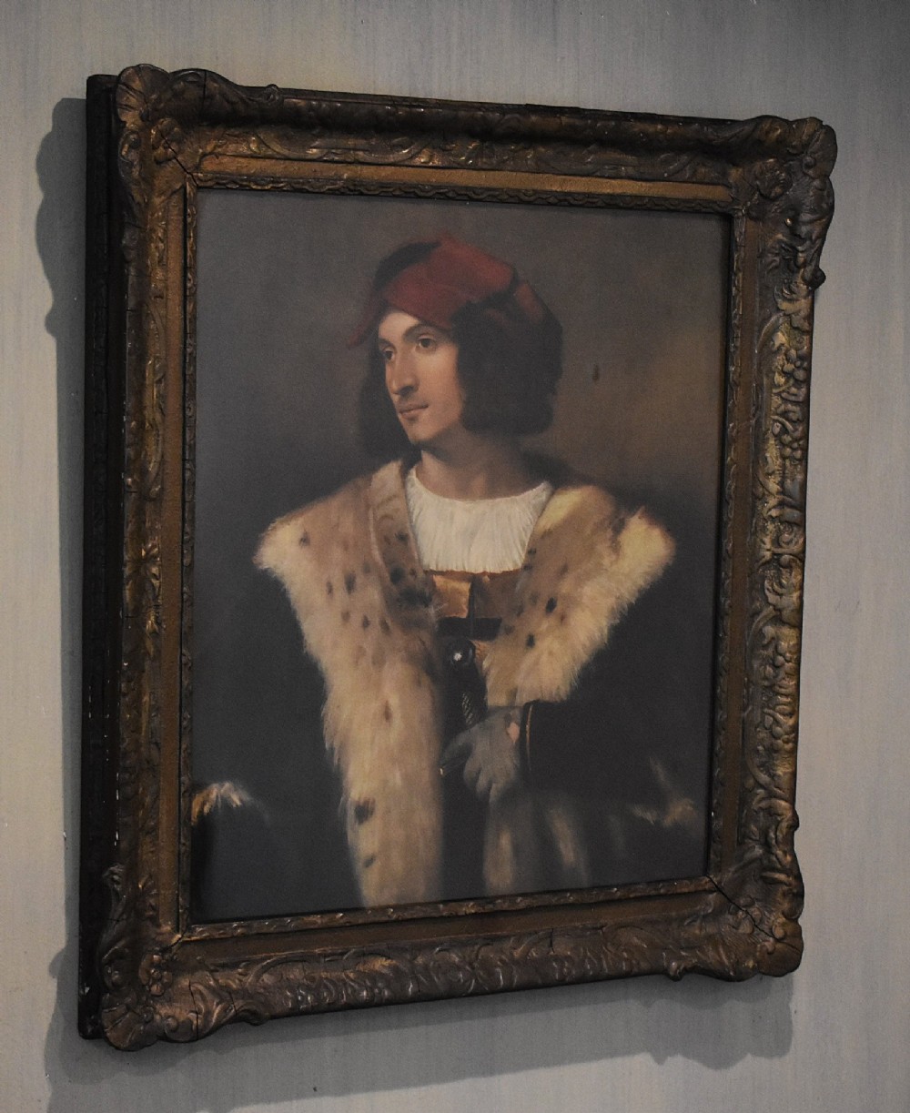 A framed portrait print depicting a young man in a red cap and fur-trimmed coat after Titian, set inside a carved gilt frame.