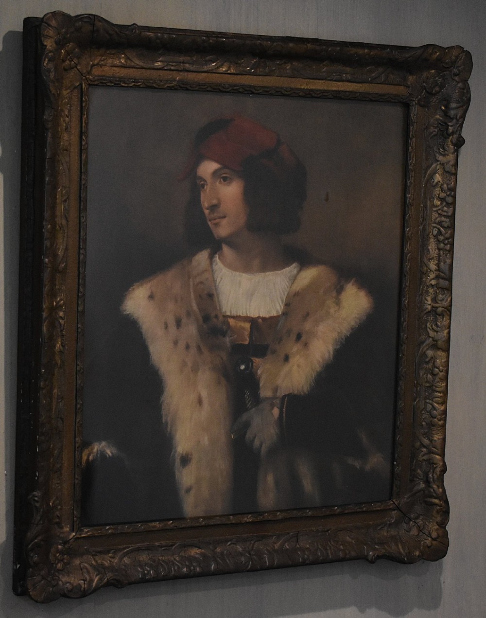 A framed portrait print depicting a young man in a red cap and fur-trimmed coat after Titian, set inside a carved gilt frame. View II