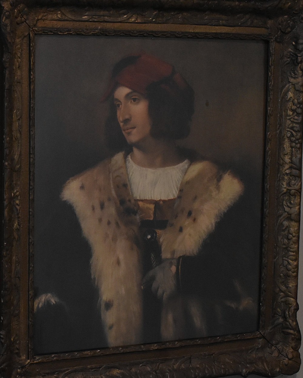 A framed portrait print depicting a young man in a red cap and fur-trimmed coat after Titian, set inside a carved gilt frame. View III