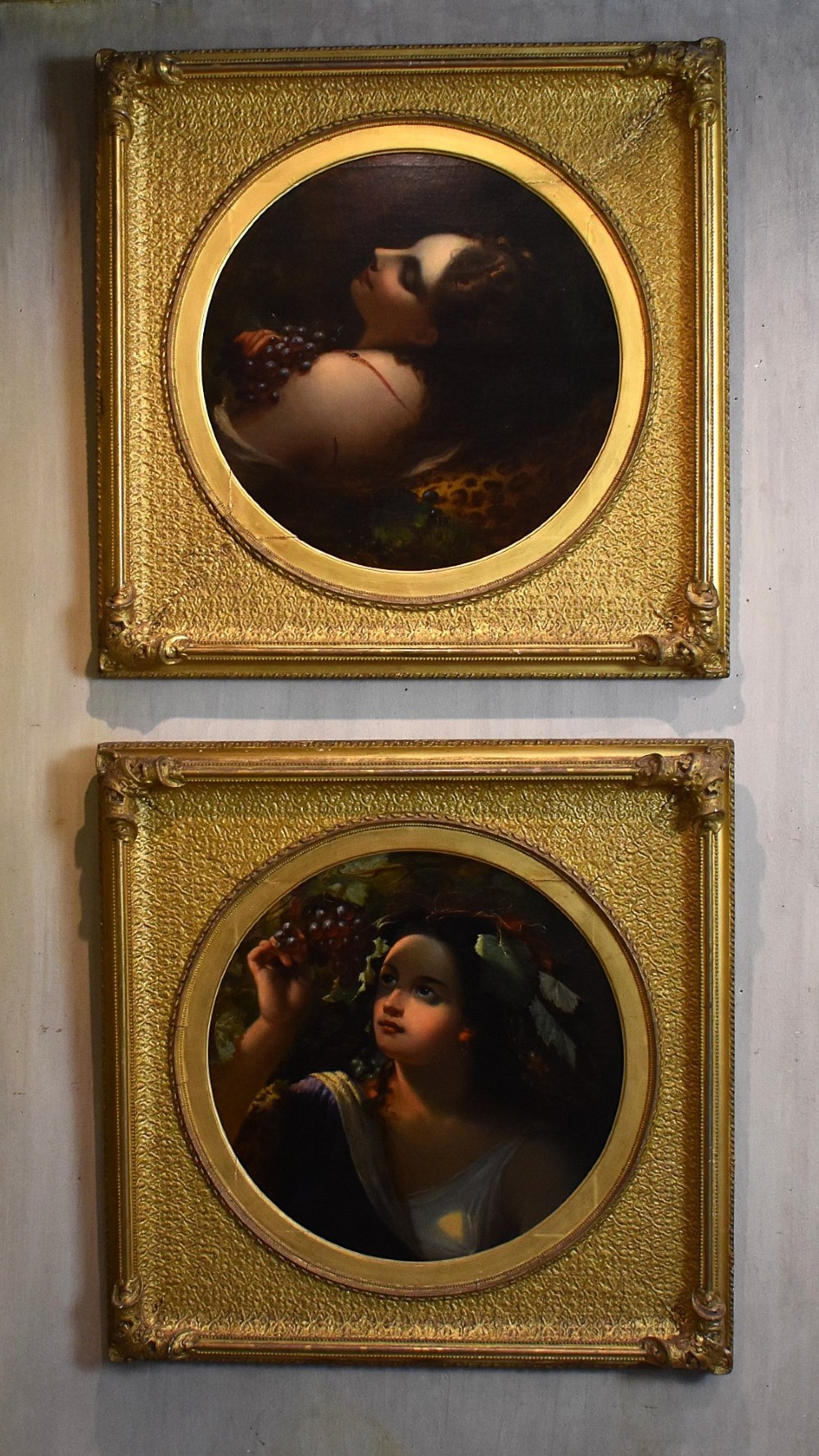 A pair of 19th-century oil paintings depicting classical female figures in circular apertures within square gilt frames.