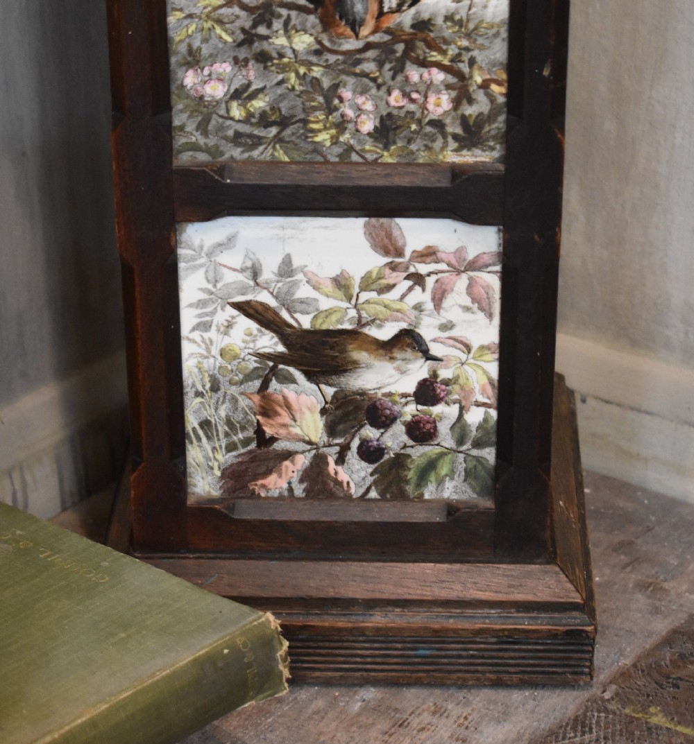 A dark wood Aesthetic Movement pedestal column with three vertical inset ceramic tiles displaying painted birds amidst foliage. View IV