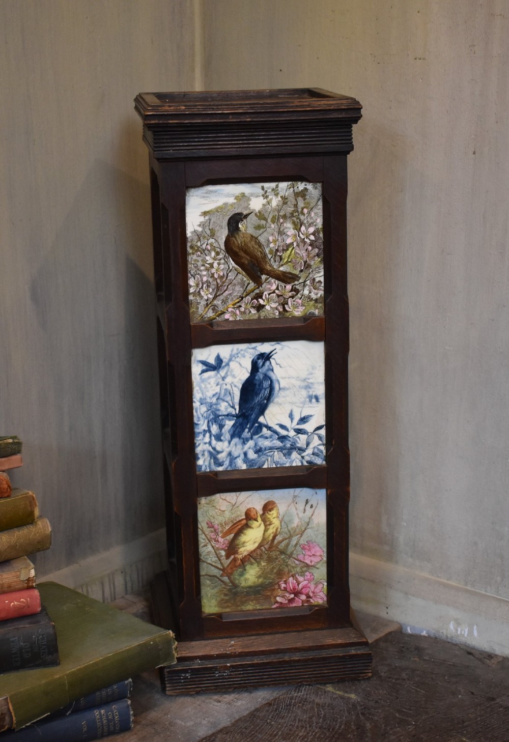 A dark wood Aesthetic Movement pedestal column with three vertical inset ceramic tiles displaying painted birds amidst foliage. View V