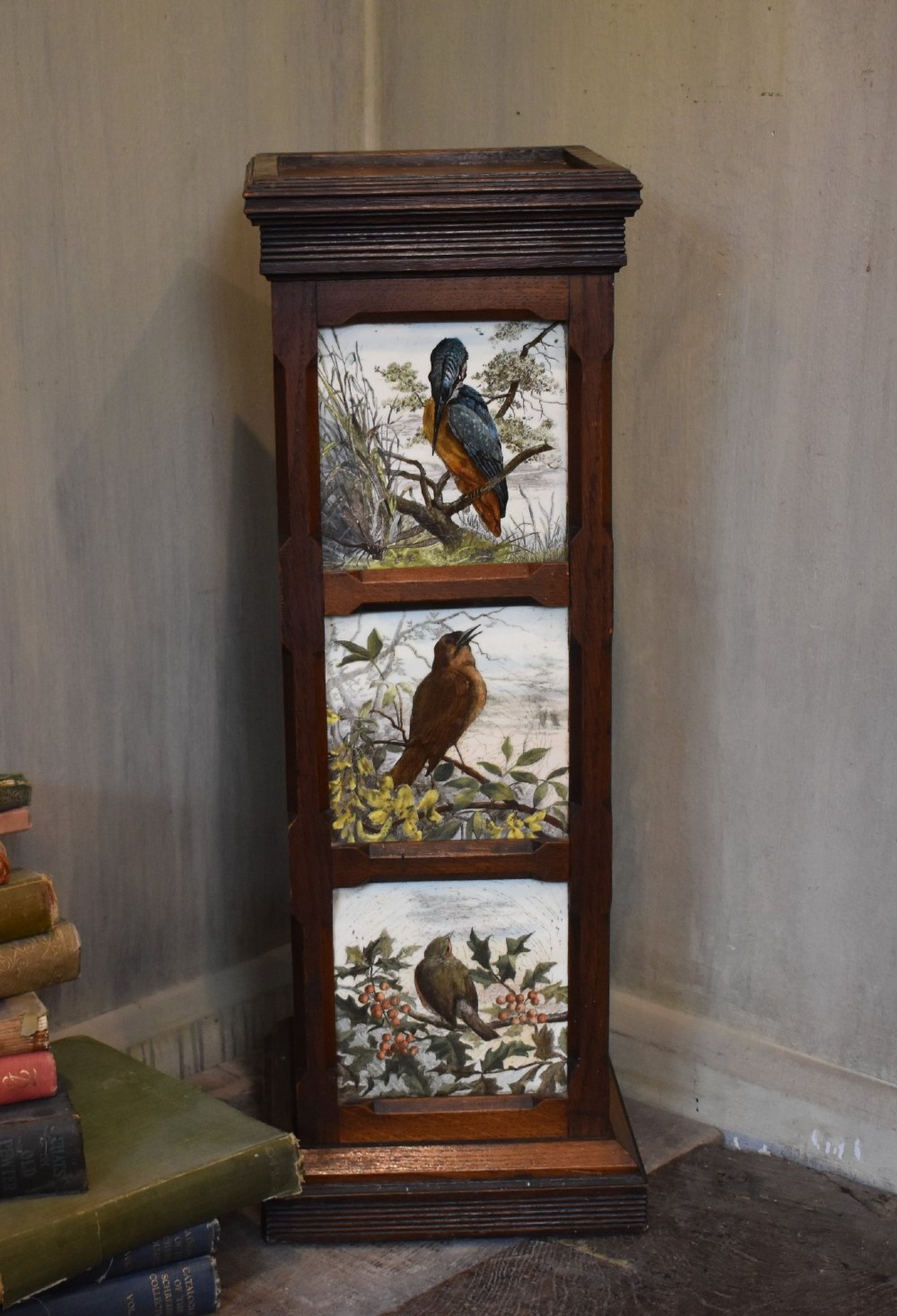 A dark wood Aesthetic Movement pedestal column with three vertical inset ceramic tiles displaying painted birds amidst foliage. View VI