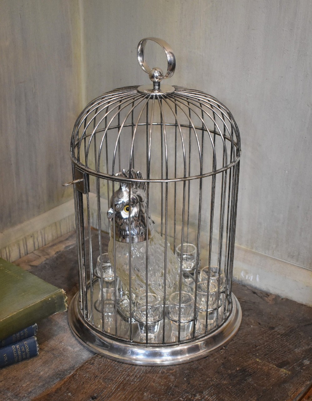 A silverplate birdcage tantalus containing a glass cockatoo-shaped decanter with a silverplate head stopper and surrounding shot glasses. View III