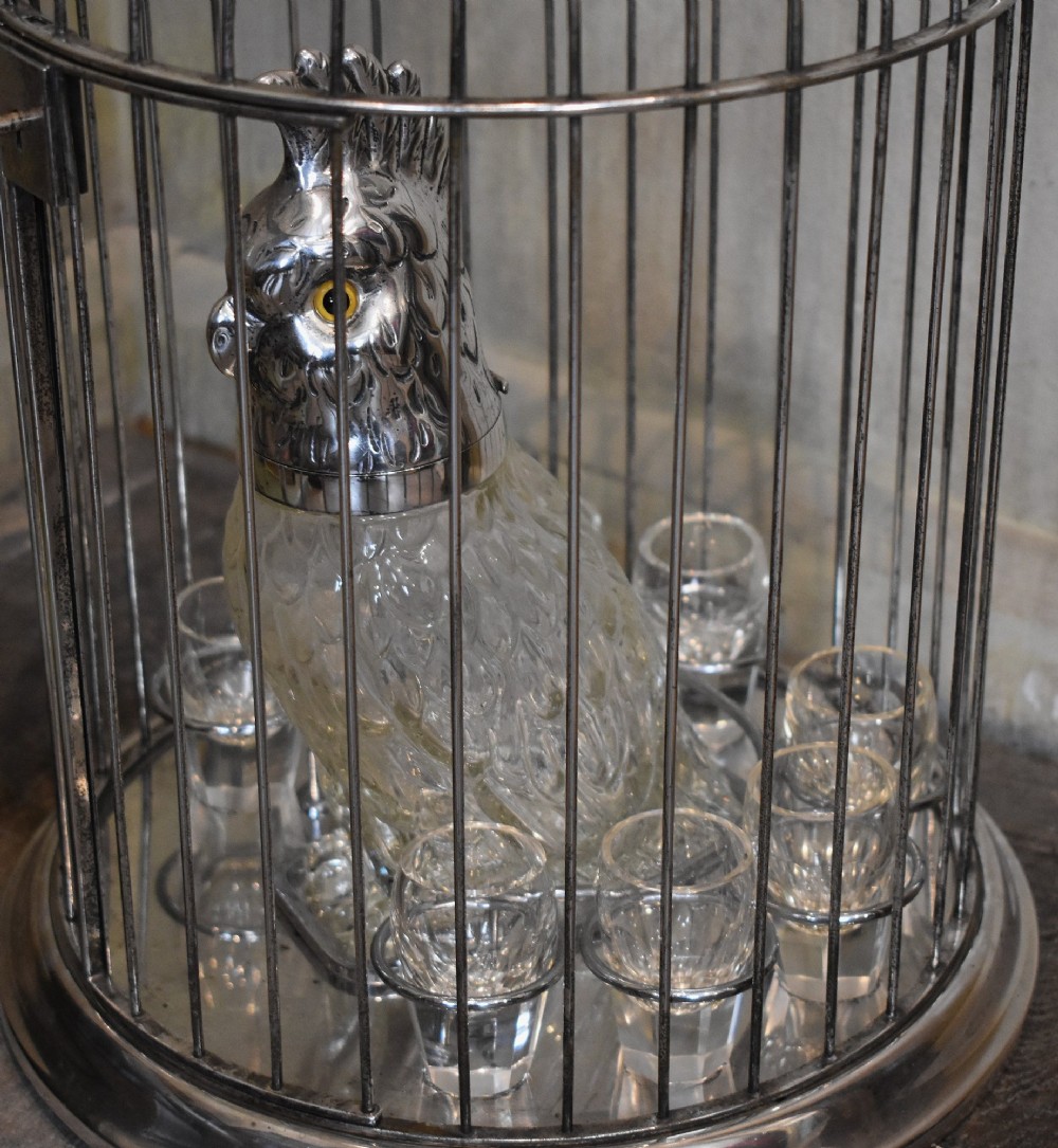 A silverplate birdcage tantalus containing a glass cockatoo-shaped decanter with a silverplate head stopper and surrounding shot glasses. View IV