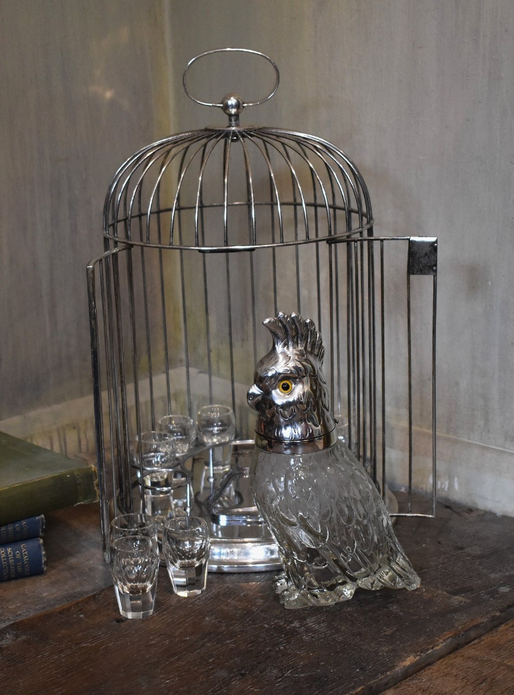 A silverplate birdcage tantalus containing a glass cockatoo-shaped decanter with a silverplate head stopper and surrounding shot glasses. View V