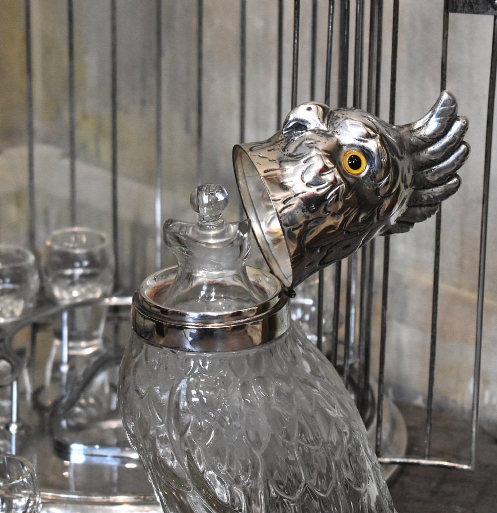 A silverplate birdcage tantalus containing a glass cockatoo-shaped decanter with a silverplate head stopper and surrounding shot glasses. View VII
