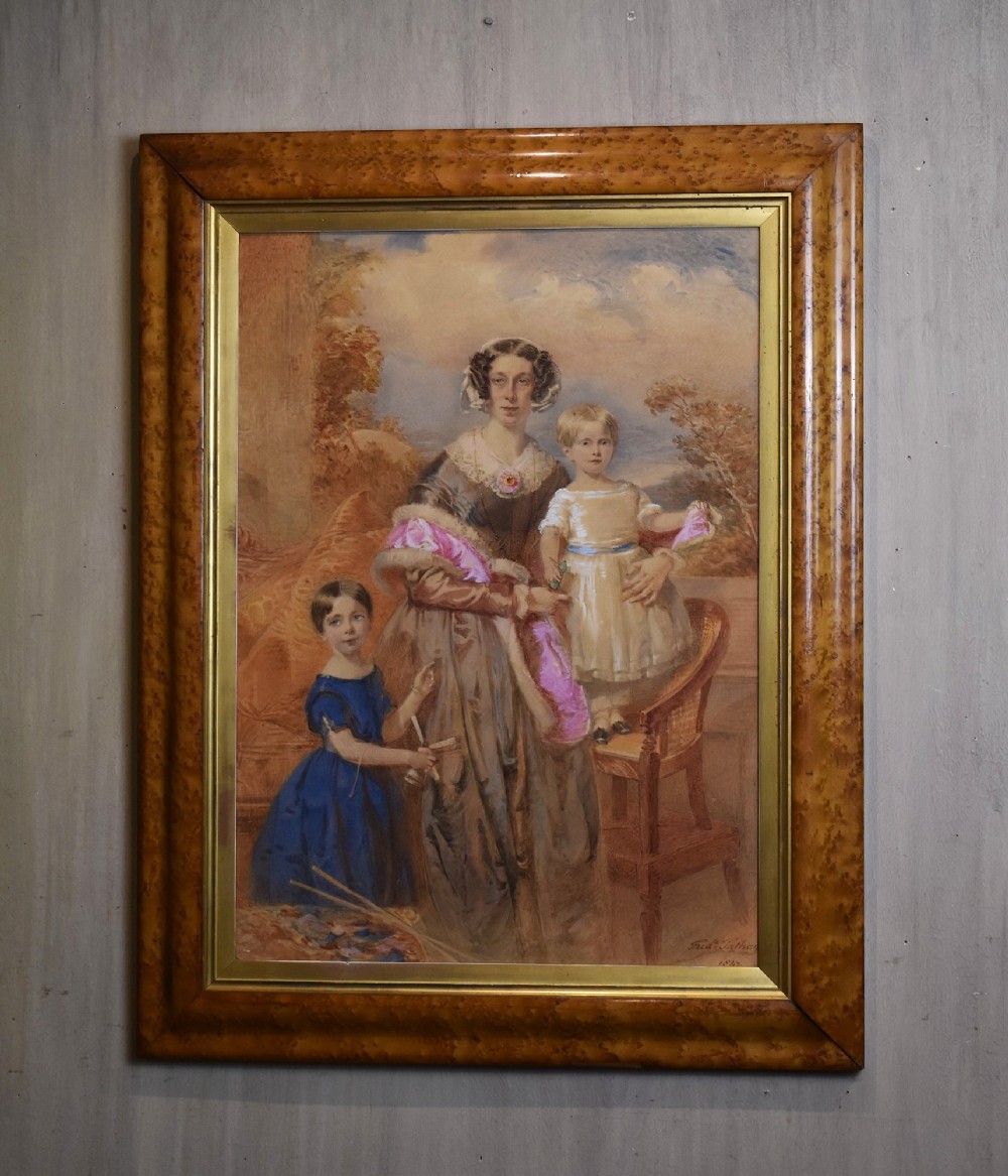 A mid-19th-century watercolour portrait depicting a mother with two young children, presented in a birds eye maple frame with a gold slip.