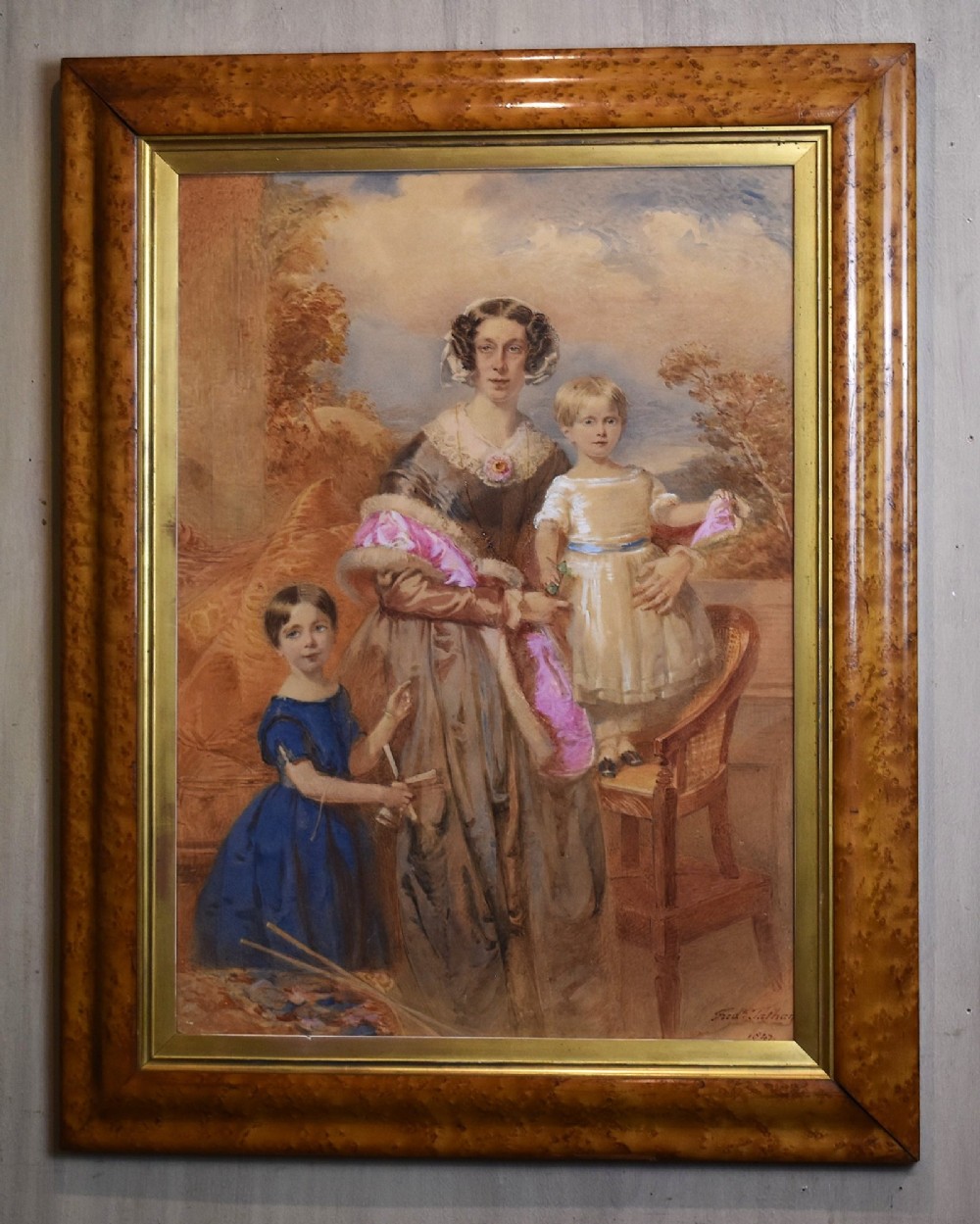 A mid-19th-century watercolour portrait depicting a mother with two young children, presented in a birds eye maple frame with a gold slip. View II