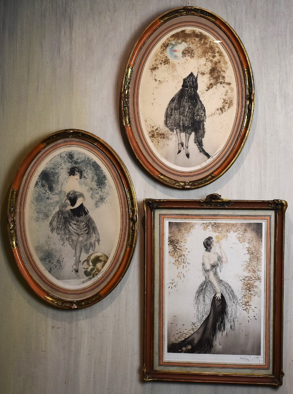 A set of three framed Art Deco fashion prints by Louis Icart featuring figures in 1920s gowns, presented in two oval and one rectangular gilt frames. View II