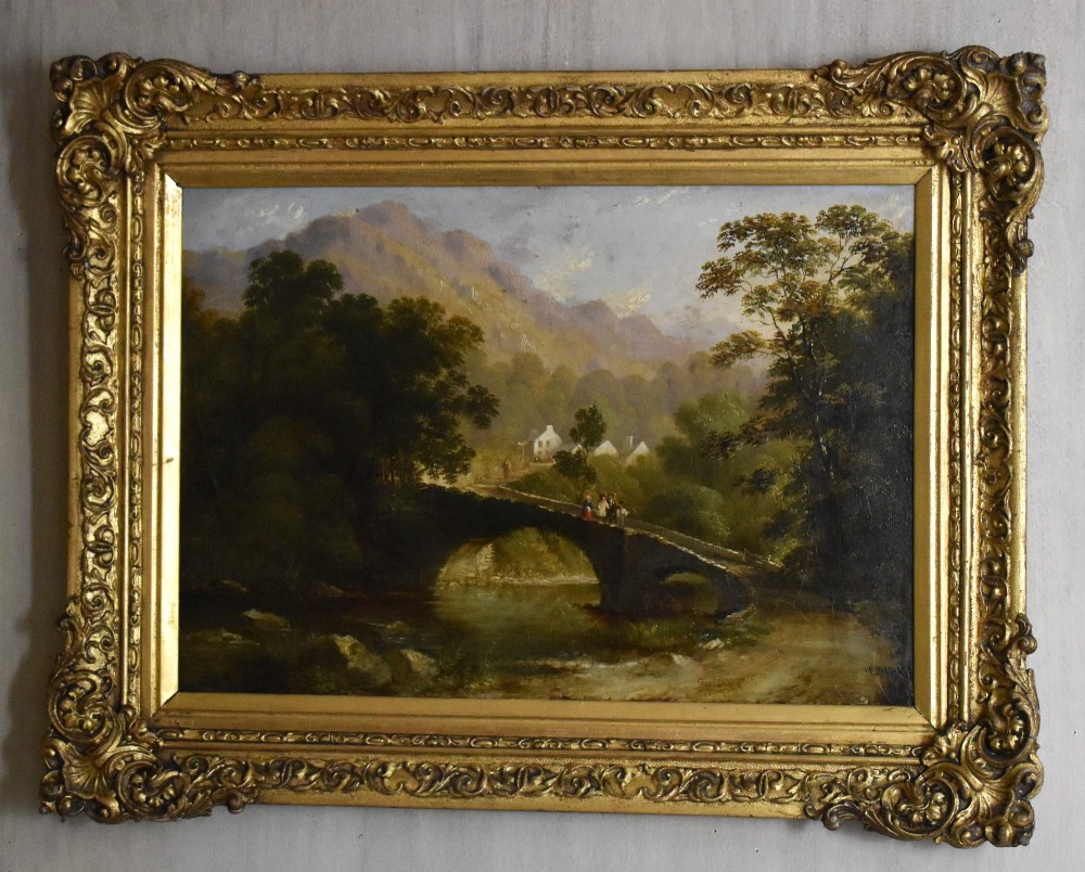 A nineteenth-century Victorian oil painting depicting a river scene with a stone arch bridge and distant mountains, housed within an ornate gilded frame. View II