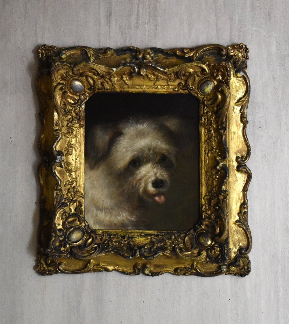 A 19th-century oil painting depicting a small terrier dog with its tongue slightly protruding, set within an ornate gilded frame.