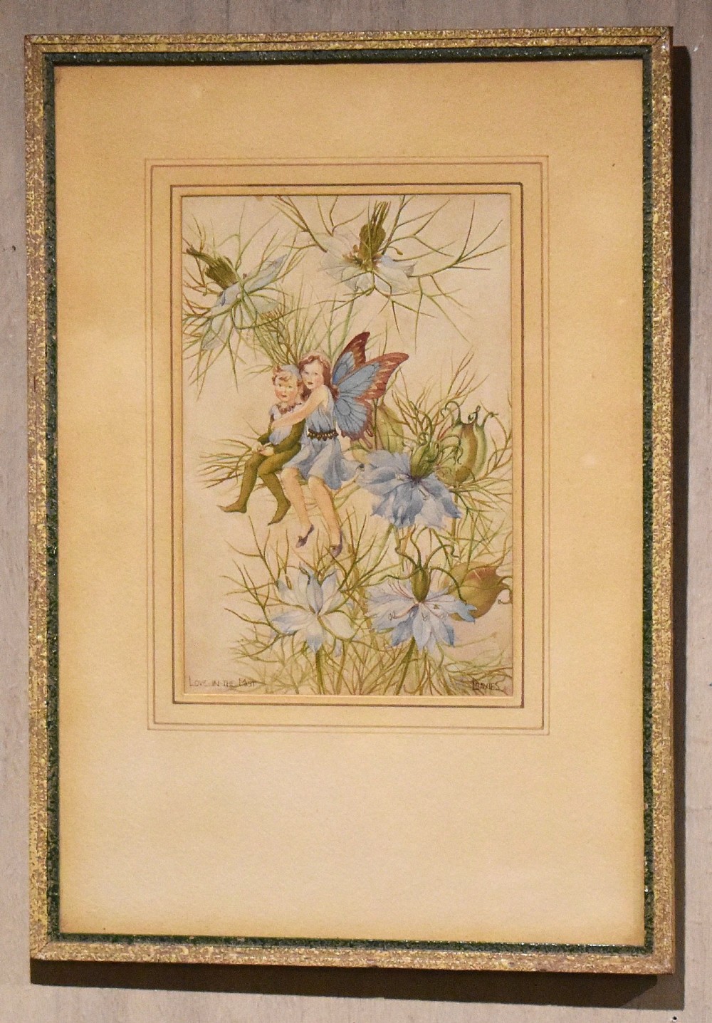 A framed watercolour illustration depicting two winged flower fairies sitting among blue love-in-the-mist blossoms, set within a double mount and a narrow gilt frame. View II