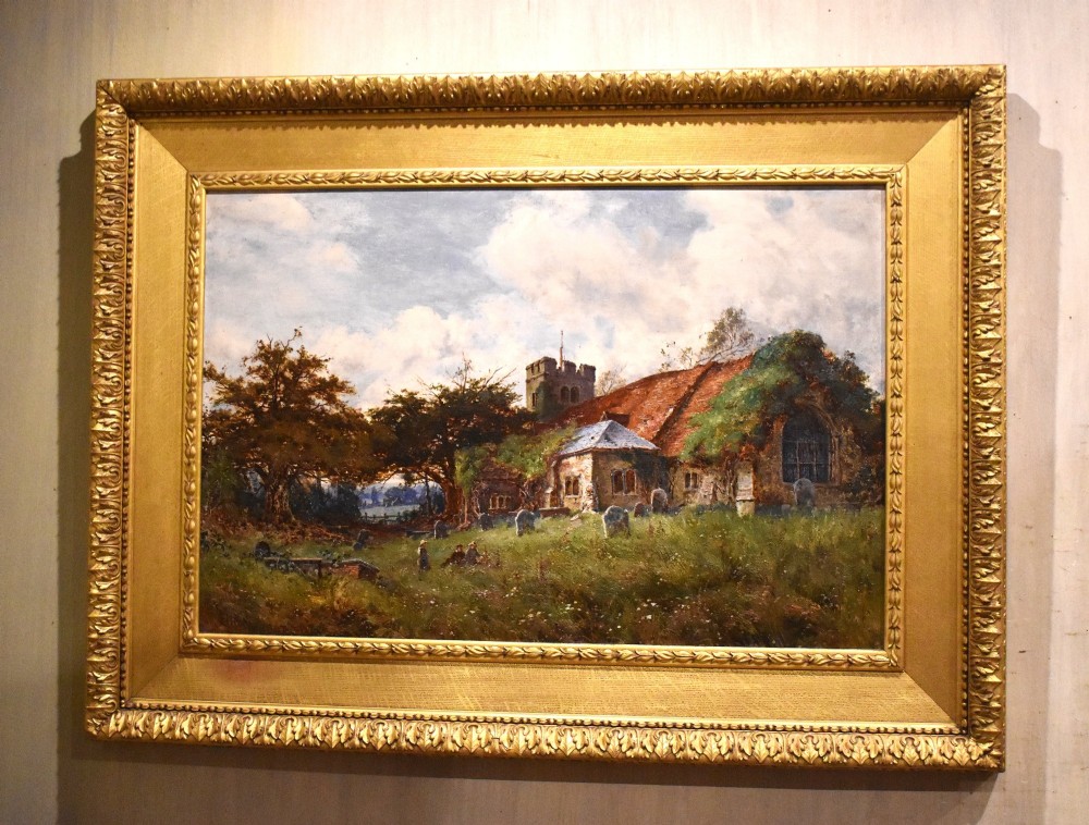 A Victorian landscape oil painting in an ornate gilded frame depicting a stone parish church and churchyard surrounded by trees under a cloudy sky.