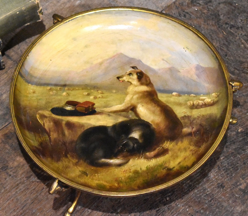 A circular Victorian papier mache comport featuring a hand-painted scene of dogs in a landscape, set within a gilt ormolu rim with decorative feet. View II