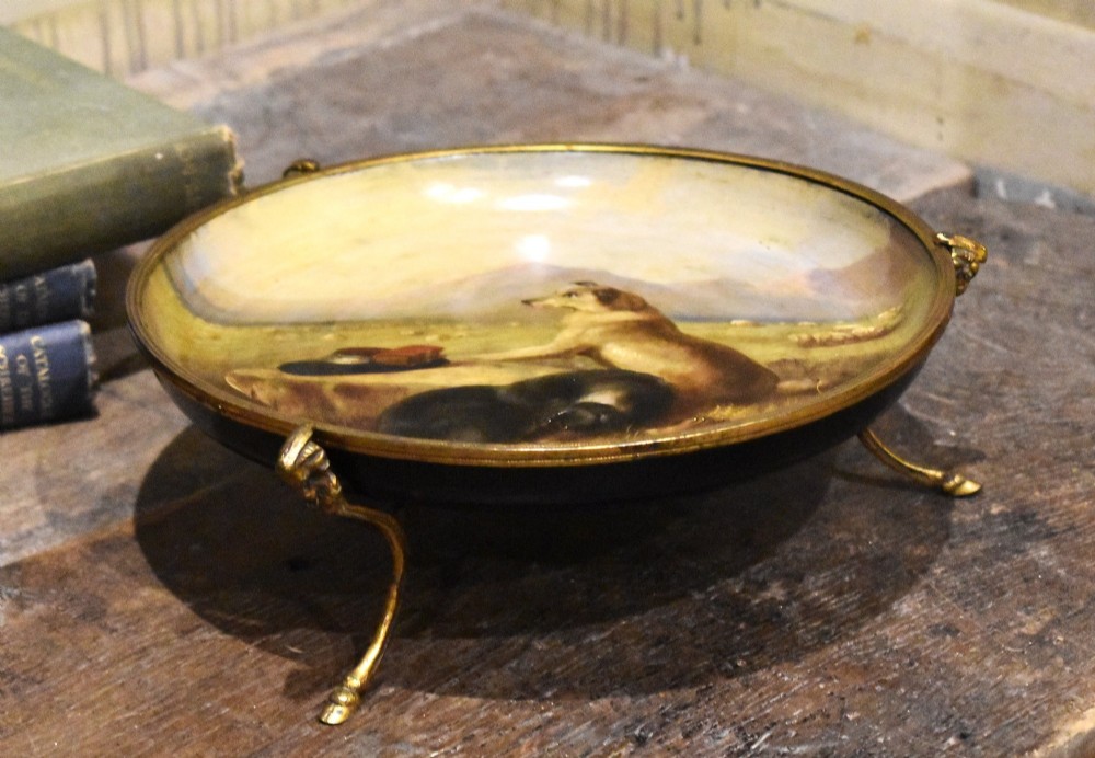 A circular Victorian papier mache comport featuring a hand-painted scene of dogs in a landscape, set within a gilt ormolu rim with decorative feet. View III