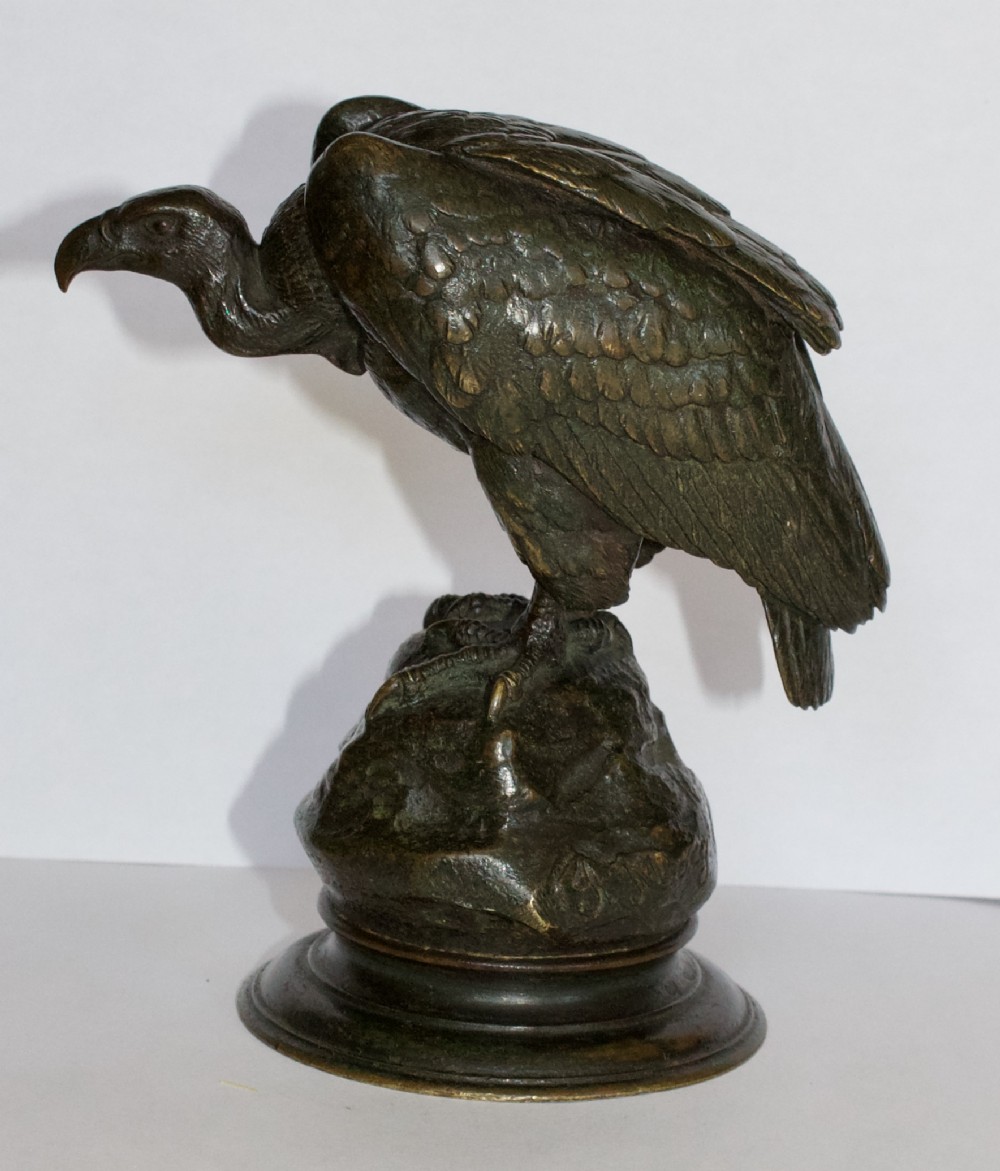 A patinated dark bronze sculpture depicting a vulture perched on a rocky base atop a rounded pedestal.