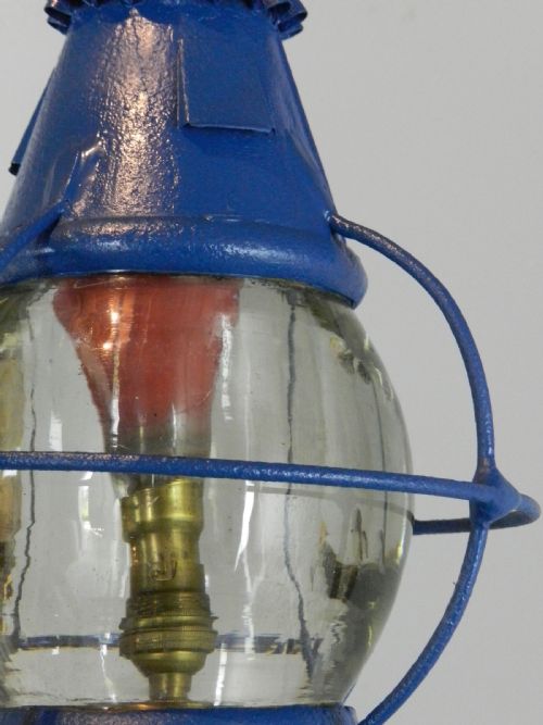 fig 1. A blue painted metal ships globe lantern with a central clear glass shade, protective wire cage, top ring handle, and electrical wiring.