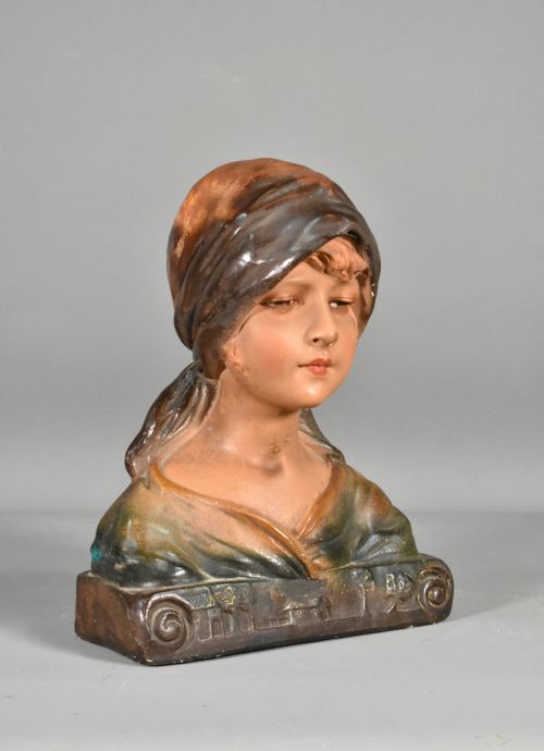 fig 1. A painted plaster portrait bust depicting a young girl wearing a draped headscarf, resting on a scrolled base.