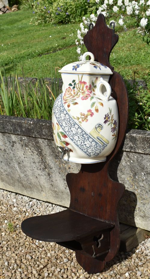 fig 2. An antique French Art Nouveau cream ceramic wall fountain decorated with botanical floral transfers and a spigot, mounted on a dark carved wooden backboard with a small shelf.