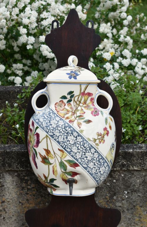 fig 3. An antique French Art Nouveau cream ceramic wall fountain decorated with botanical floral transfers and a spigot, mounted on a dark carved wooden backboard with a small shelf.