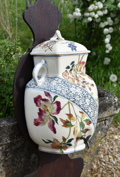 fig 4. An antique French Art Nouveau cream ceramic wall fountain decorated with botanical floral transfers and a spigot, mounted on a dark carved wooden backboard with a small shelf.