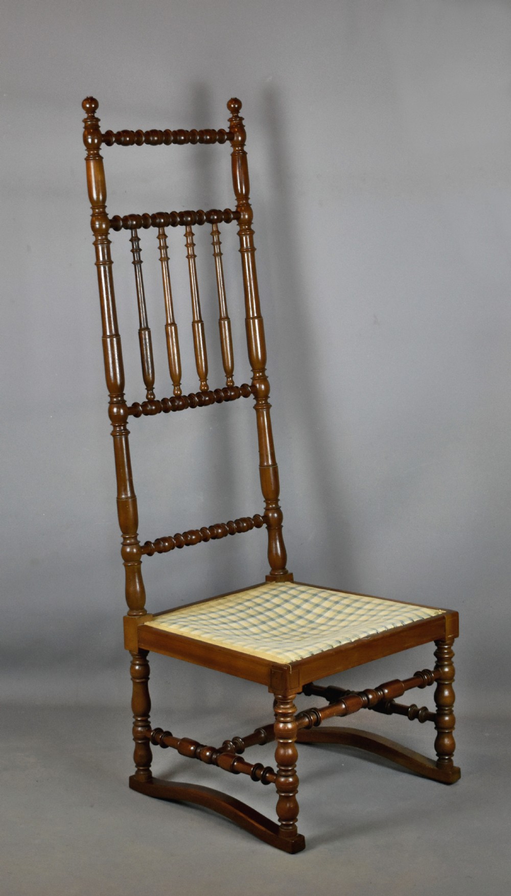 An antique French walnut nursing chair featuring a tall bobbin-turned backrest, turned legs, and a checked upholstered seat. View III