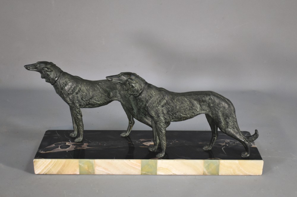 An Art Deco patinated metal sculpture depicting two Borzoi dogs standing on a layered black marble and cream onyx plinth.